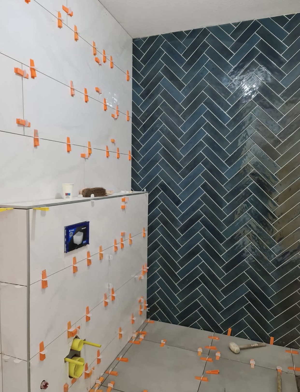 Badkamer met petrolblauwe visgraat accentwand en witte glanzende wandtegels — tegelzetter Noord-Holland