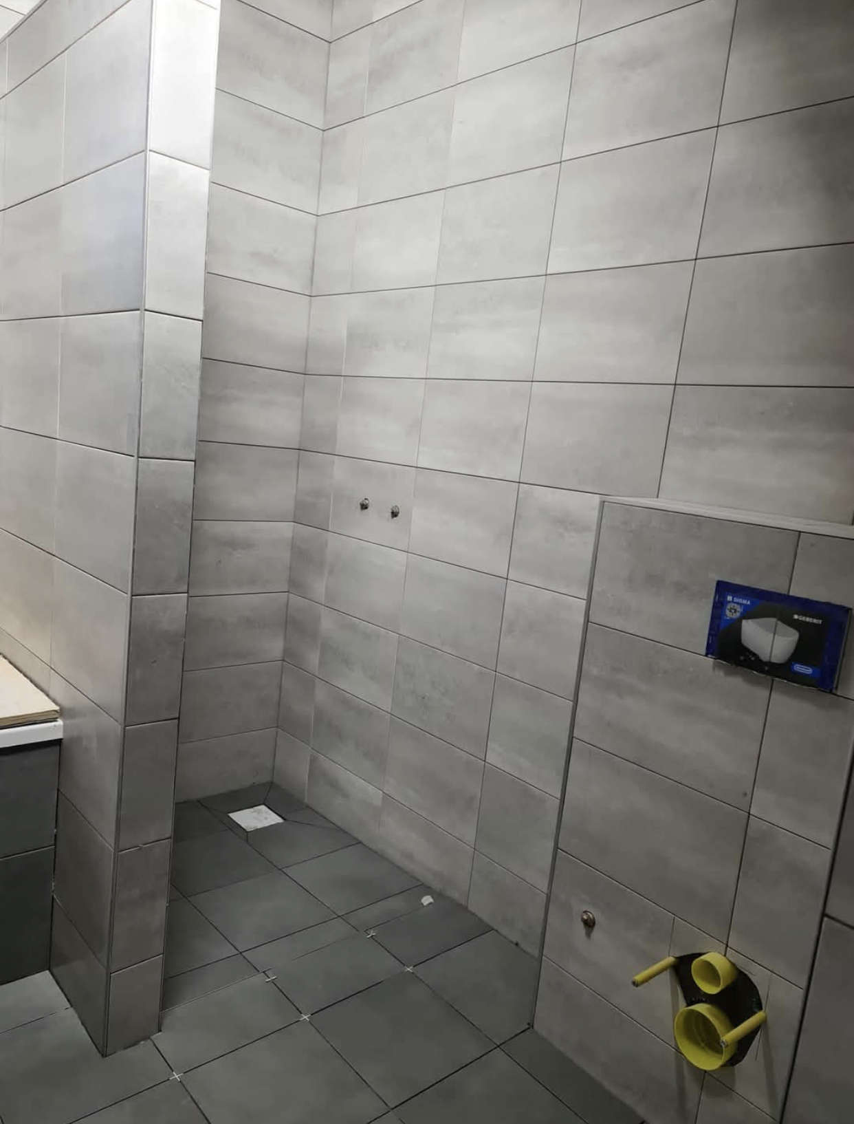 Strak betegelde badkamer met lichte betonlook wandtegels en grijze vloertegels — tegelzetter Noord-Holland