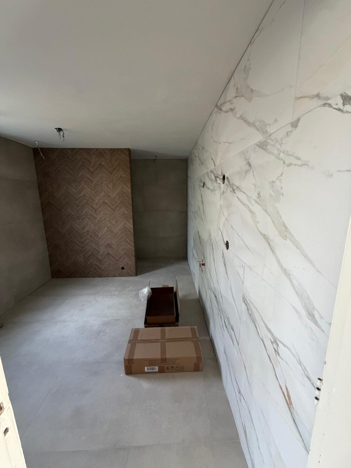 Luxe badkamer met marmerlook tegels en houten visgraat accentwand — badkamerrenovatie Noord-Holland