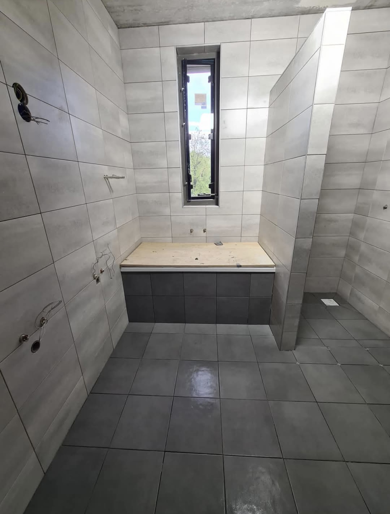 Badkamer met lichte betonlook wandtegels en antracietgrijze vloertegels — tegelzetter Noord-Holland